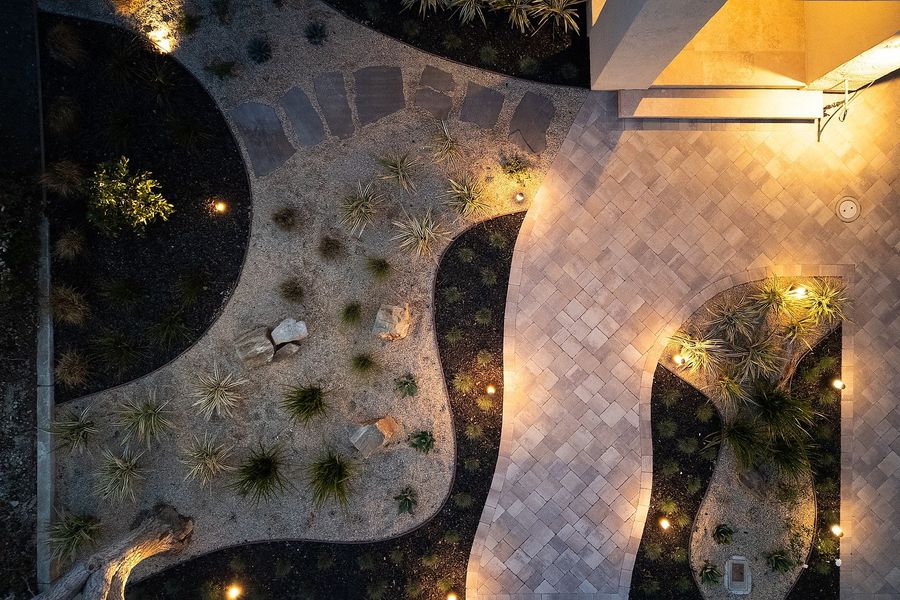 Overhead view of curving gravel beds with grasses and boulders, a flagstone stepping path and the paver court, lit at dusk