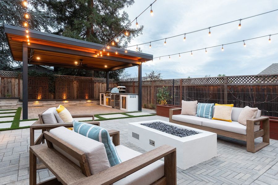Dusk view of the herringbone court with fire table, sofas, string lights and the lit steel pavilion beyond