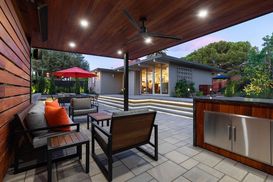 View from under the pavilion roof toward the lit house, with a built-in stainless storage cabinet and lounge chairs