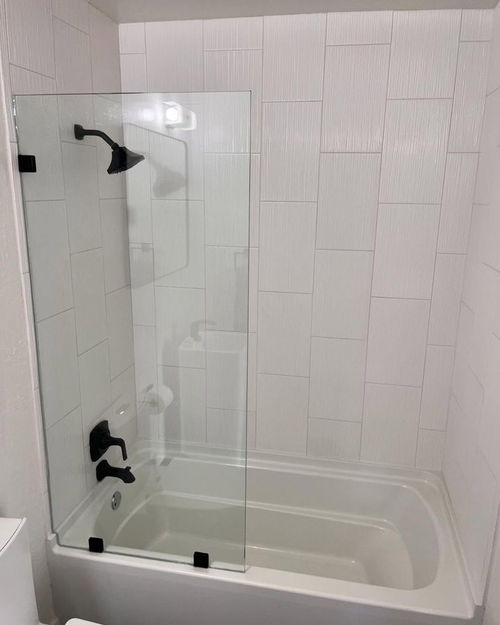 Frameless glass panel over a bathtub with black fixtures