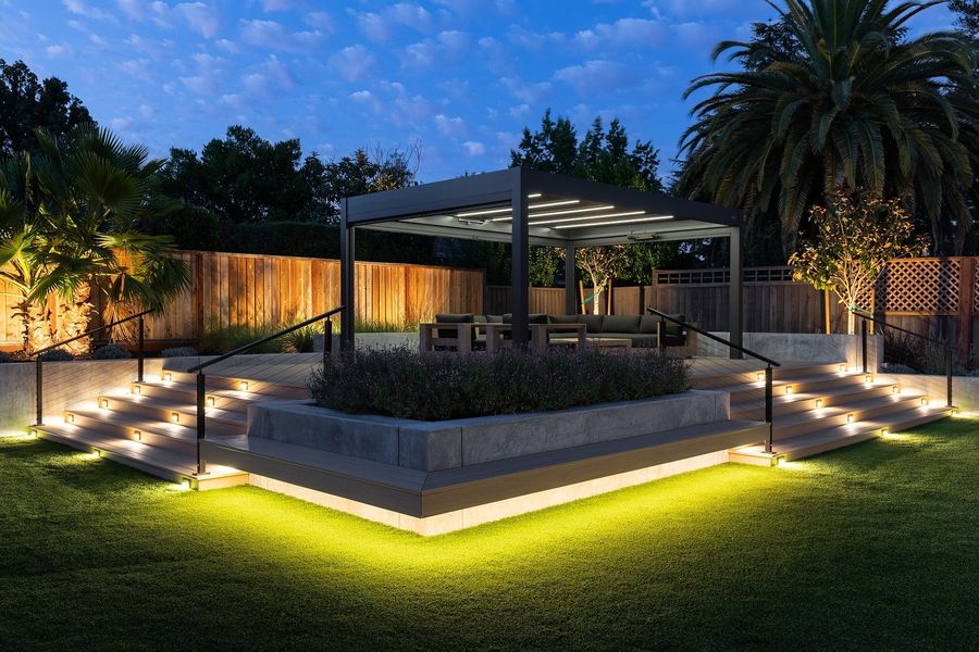 Twilight view of the lit staircase and planter with a glowing green under-edge light and the pergola behind