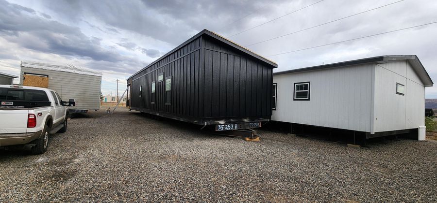 Dark modular home with a white unit beside it on a gravel pad