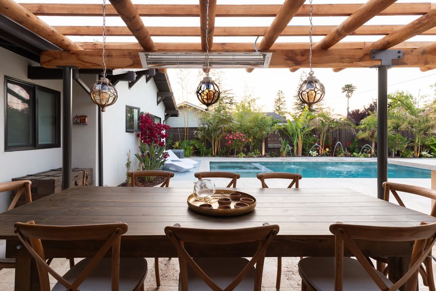 Covered dining terrace under rough-sawn timber beams, hanging lanterns above the table