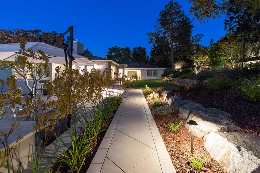 Paved walkway at dusk between planted beds of grasses and boulders