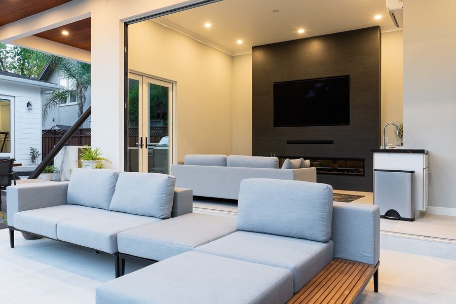 Cabana lounge at dusk with light grey sofas facing a dark feature wall with a linear fireplace and a mounted screen
