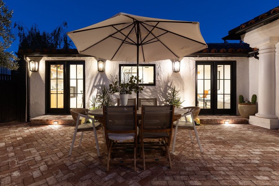 Twilight view of a dining table under an umbrella in front of the lit back doors of the house