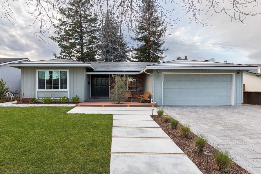 Front of a single-storey house with a lawn, a walkway of wide rectangular concrete pavers, ornamental grasses in mulch and a grey paver driveway
