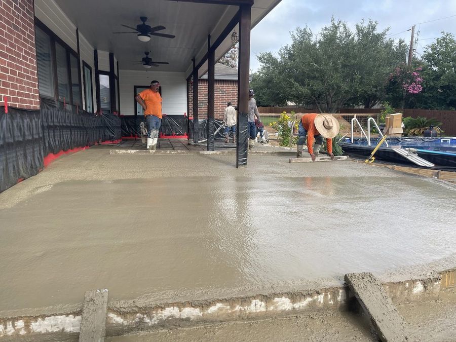 Crew screeding fresh concrete for a large slab beside a backyard pool under a covered patio