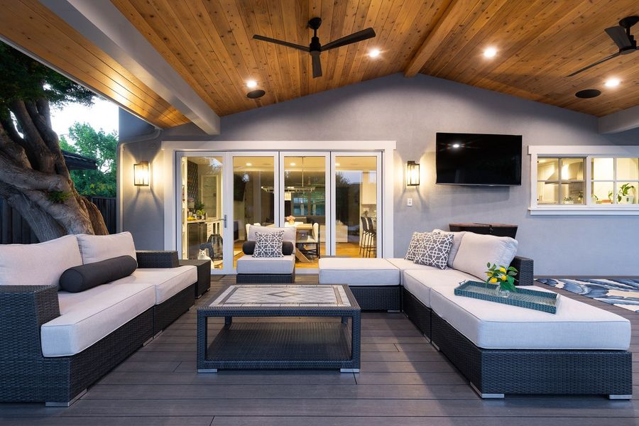 Sectional sofa and coffee table on a gray composite deck facing a folding glass door wall and a wall-mounted TV, under a cedar ceiling