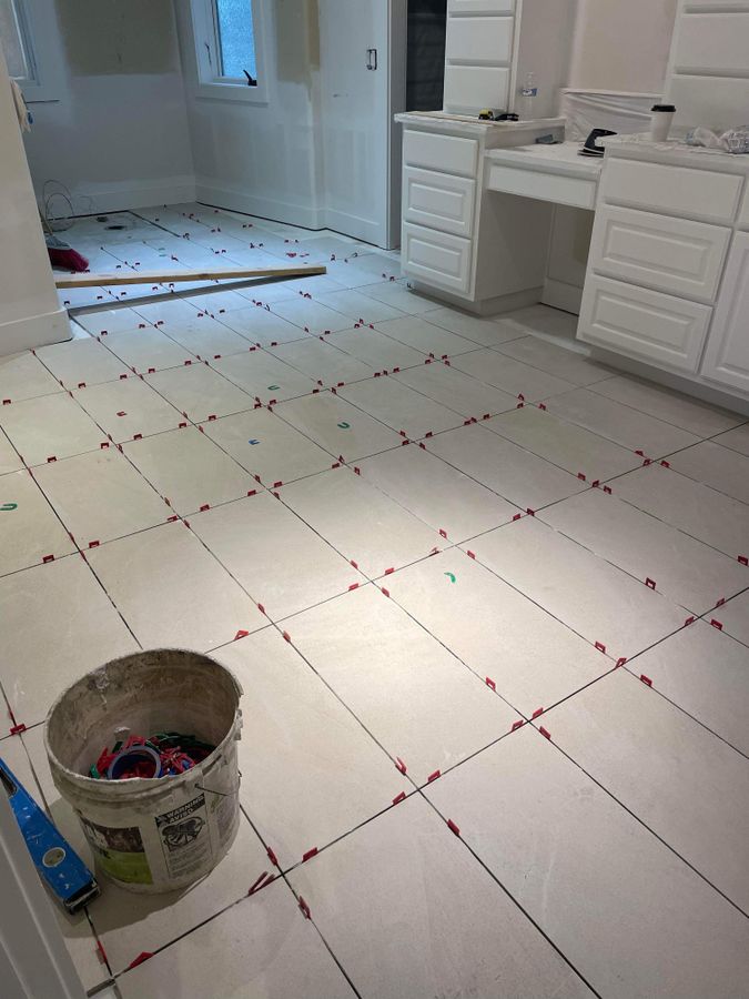 Large-format white floor tile set with leveling clips in a bathroom