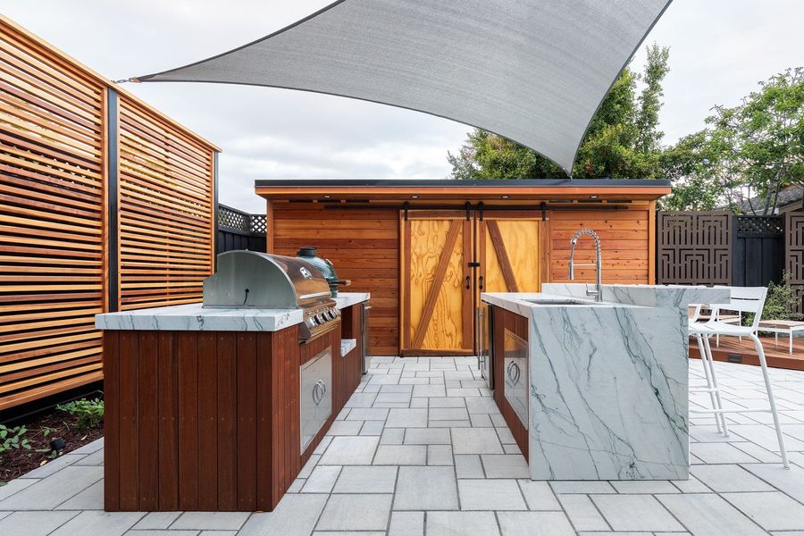Built-in grill with ipe cabinet and waterfall-edge stone counter beside a cedar cabinet with sliding barn doors