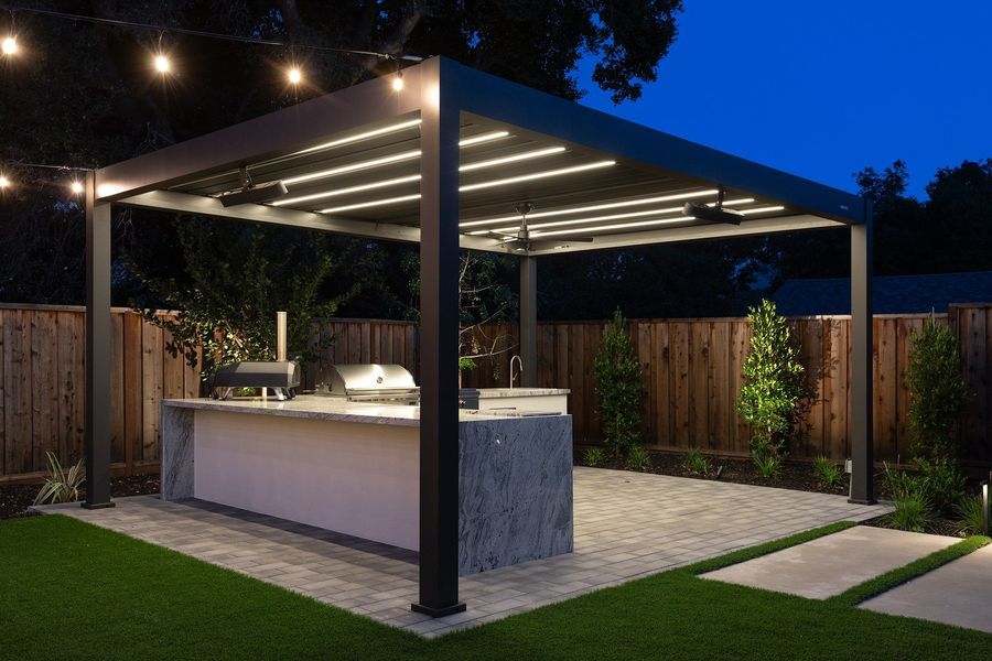 Angled night view under the pergola with glowing strip lights, a ceiling fan and string lights over the kitchen island