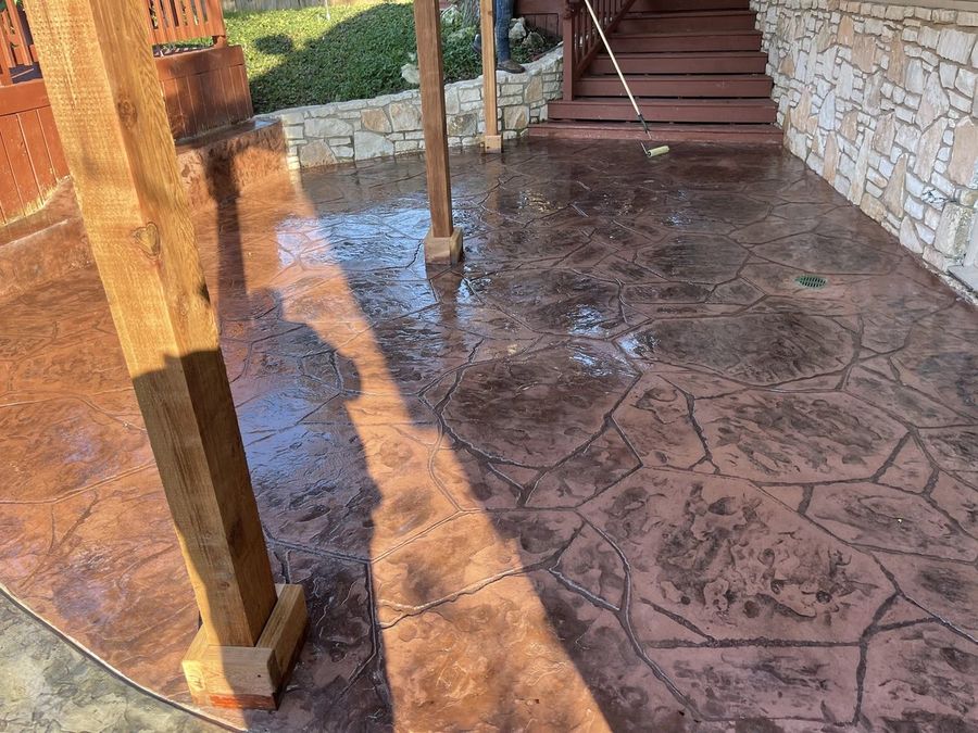 Stamped flagstone-pattern patio in warm earth tones being sealed under a covered porch