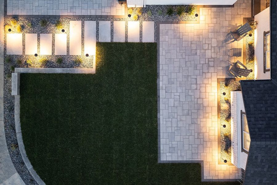 Top-down twilight view of the paver patio and stepping-slab path with warm garden lights around the lawn