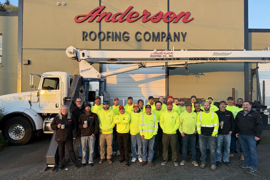 The Anderson Roofing crew gathered in front of the company shop beside a boom truck