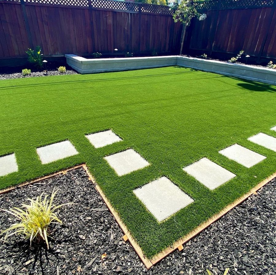 Close view of rectangular concrete stepping pavers set in green lawn beside a mulch bed with a small ornamental grass and wood edging.