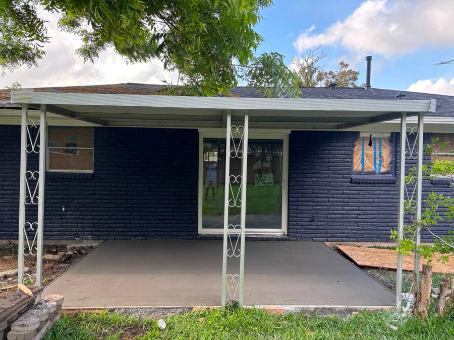 Concrete slab poured under a metal patio cover against a dark brick house