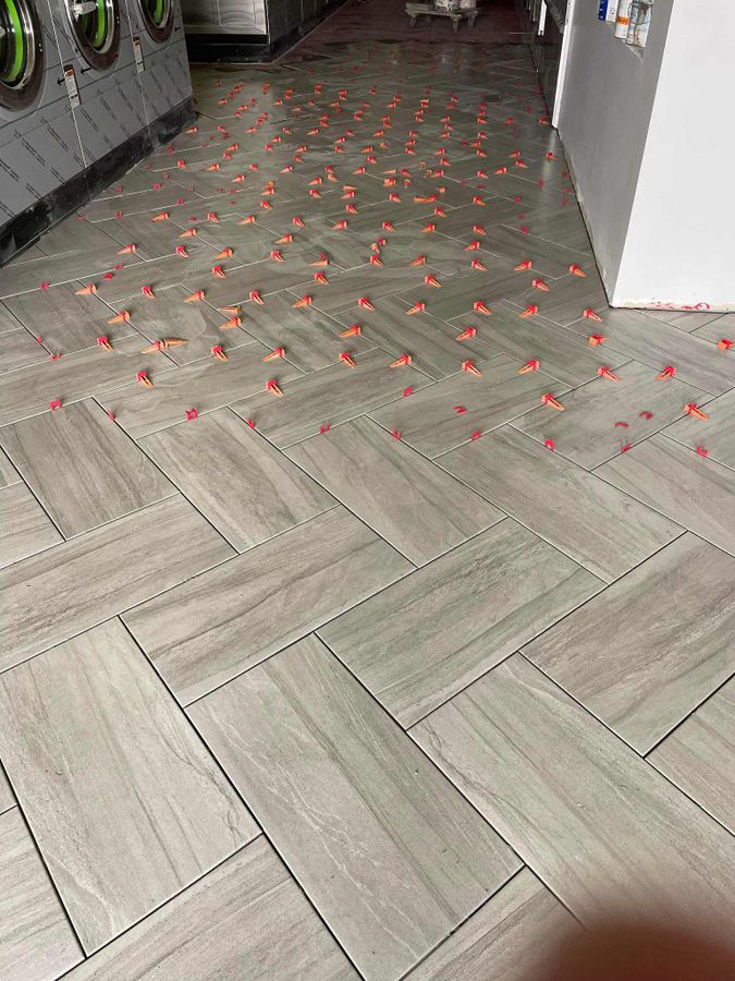 Gray herringbone plank tile floor with leveling clips in a laundry room