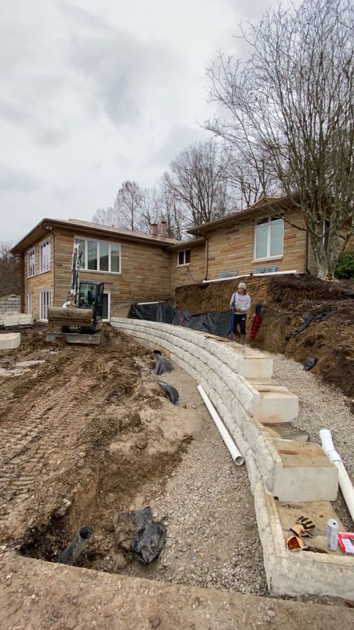 White drainage pipe laid along the base of a block wall with the soil cut open beside it