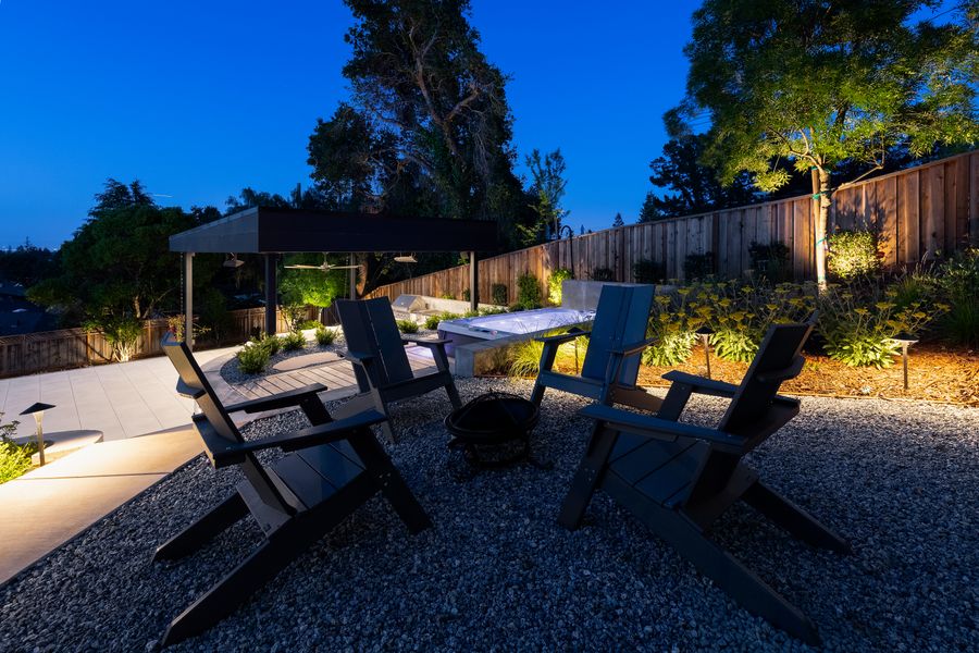 Chairs set around a fire bowl on the gravel court at dusk, pavilion lit behind