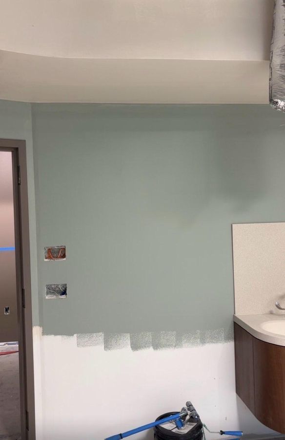 Interior wall being repainted a soft green above fresh white primer, with the ceiling already painted