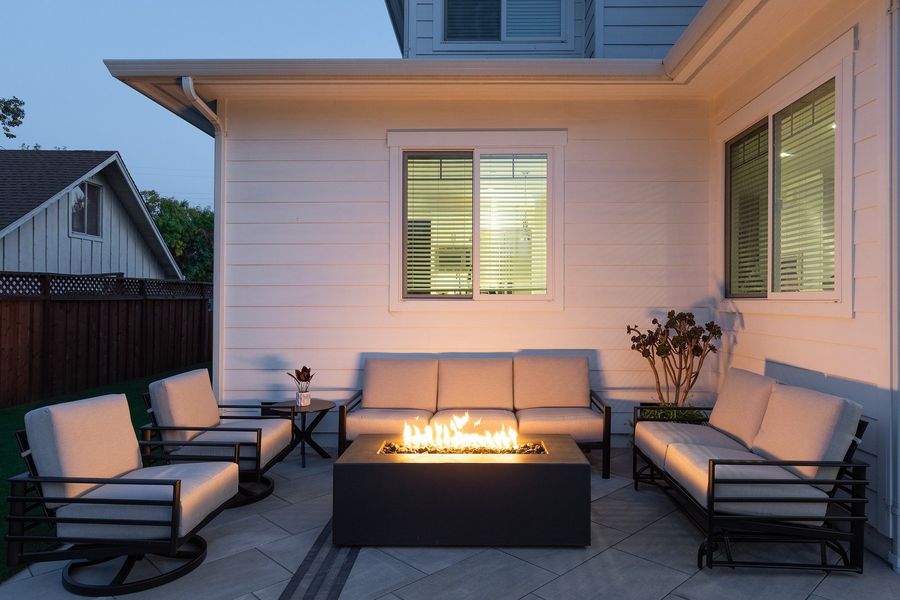 Linear gas fire table alight between a sofa and chairs against the white house wall at dusk