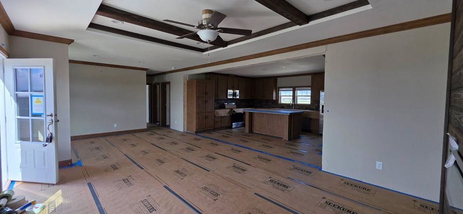 Living room with a tray ceiling and wood beams, floor covered in protection paper
