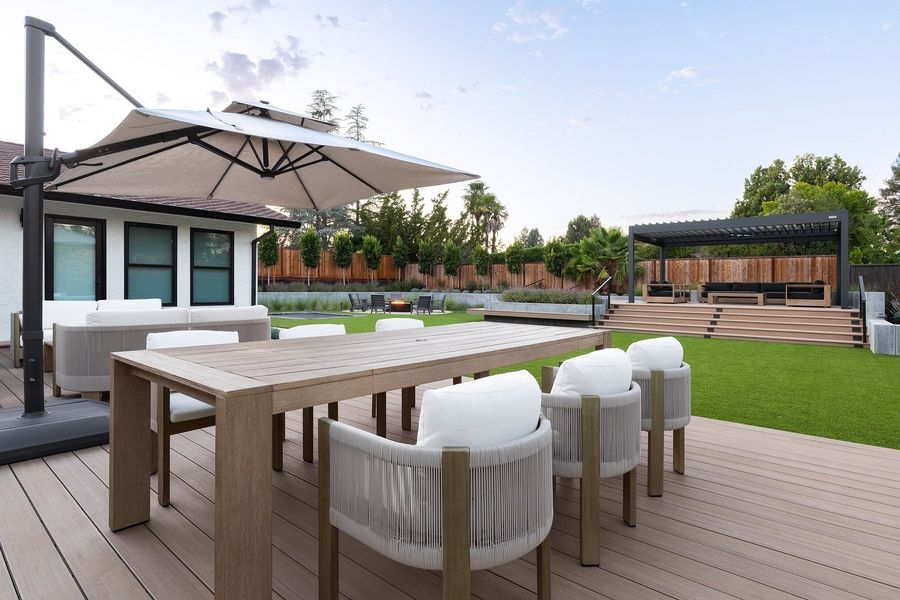 View across the house deck with white sofas in the foreground and the distant pergola deck across the lawn