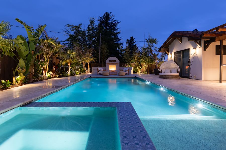 The pool lit from within at dusk, raised spa at the near end, patterned tile terrace alongside