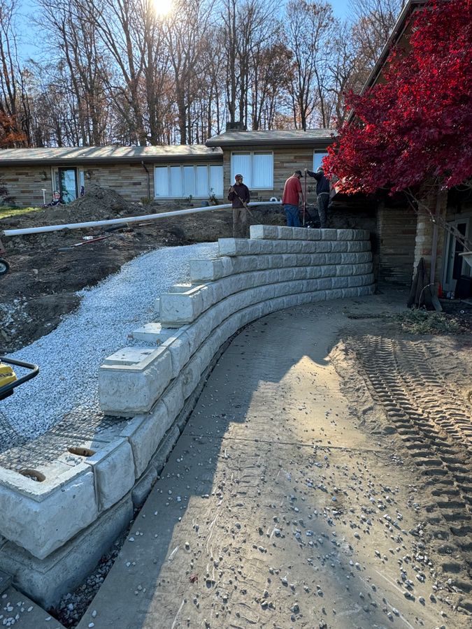 Crew members at the top of a curved block wall with gravel filled in behind it