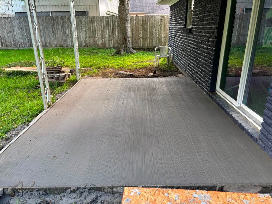 Broom-finished concrete patio slab beside a back door and open lawn