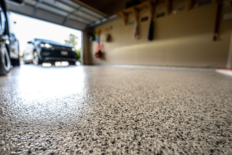 Close view of a speckled flake epoxy floor with a car parked beyond the open garage door
