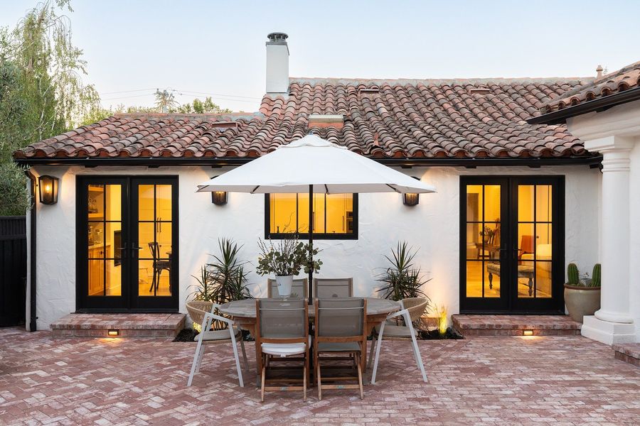 Dining table and umbrella on a herringbone brick patio in front of the back doors, with step lights in the brick risers