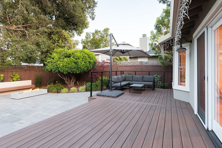 Wood-look deck with a black cable railing, an outdoor sectional under a cantilever umbrella, and pavers beyond