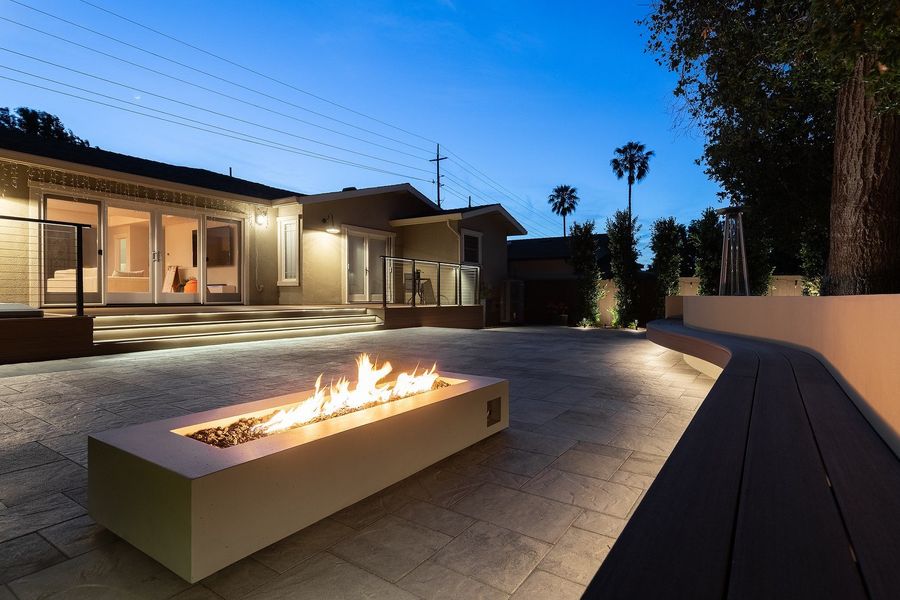 Fire table burning in the foreground, with the lit deck steps and the house glowing in the background at dusk