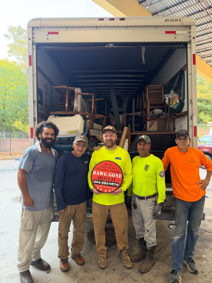 The Dawg Gone Move It crew in work shirts standing in front of an open 20-foot box truck, holding the company's round door magnet
