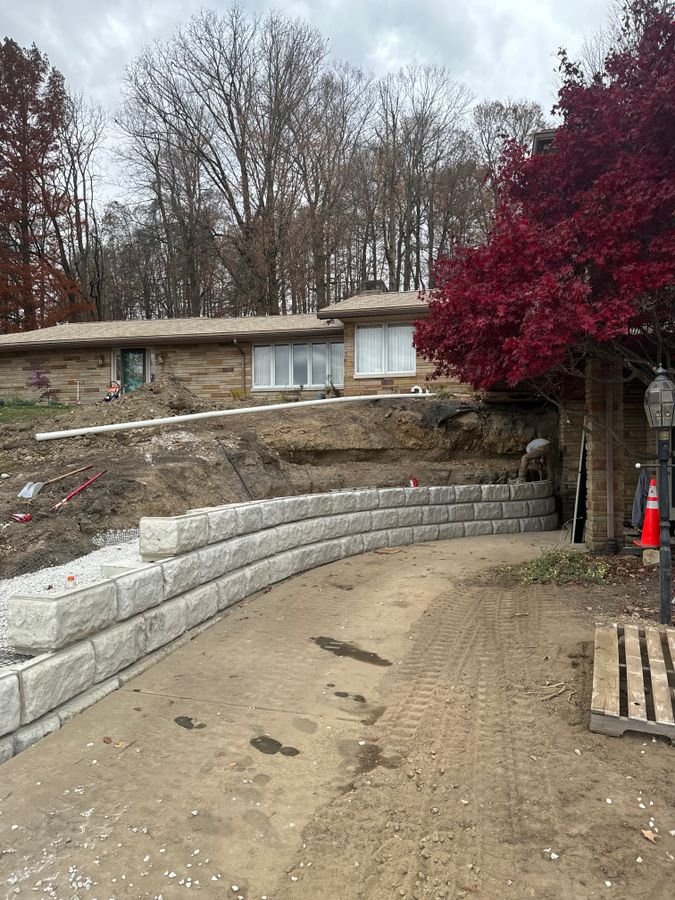 Curved block wall taking shape along a driveway with a white pipe running along the cut above it