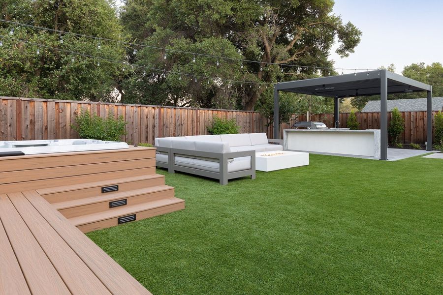 Raised timber-toned deck with steps beside a lawn, a white sofa and a low fire table beyond