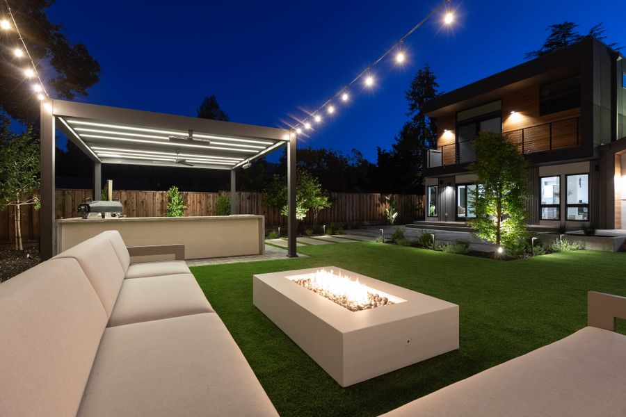 The concrete fire table alight on the lawn edge at dusk, string lights overhead