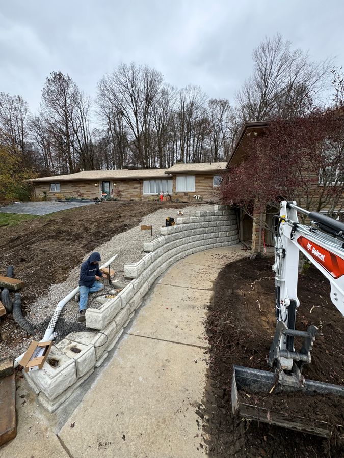 Excavator and a crew member working along a block wall in progress
