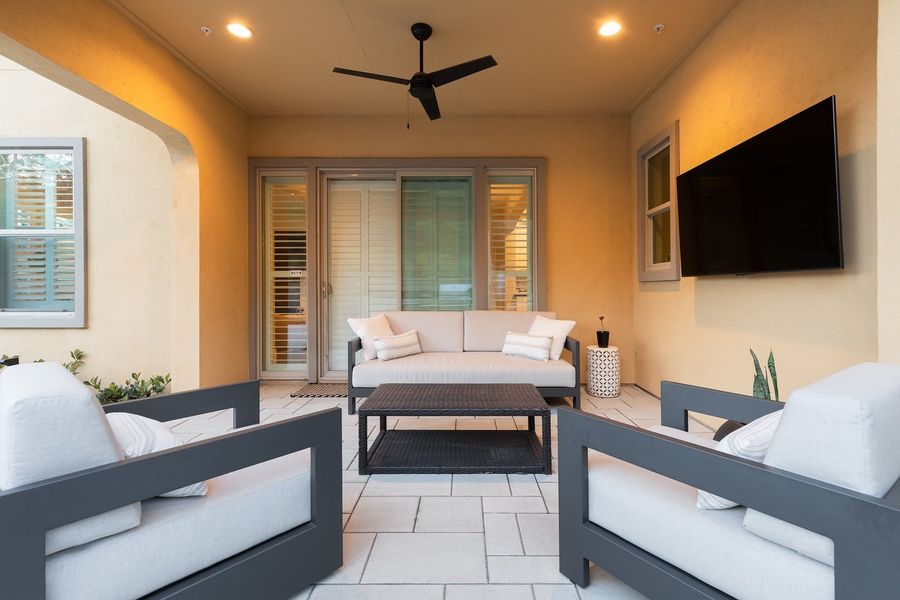 Covered patio with a ceiling fan, wall screen, outdoor sofa and armchairs seen from the paver terrace