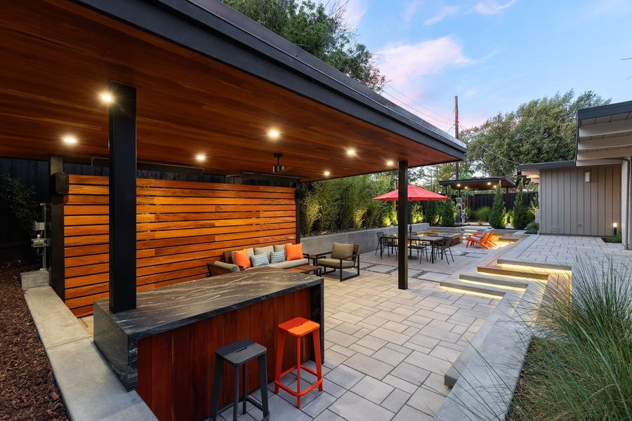 Stone-topped bar with orange stools under the wood-lined pavilion roof, with lit steps and the dining terrace beyond
