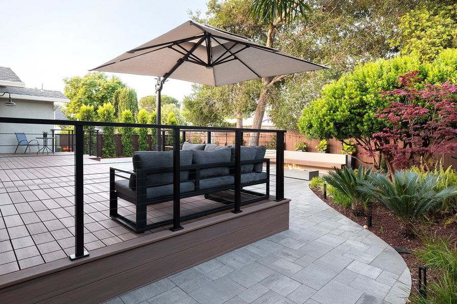 Japanese maple, sago palms and ferns beside a curving paver path and the cable-rail deck with a sectional sofa