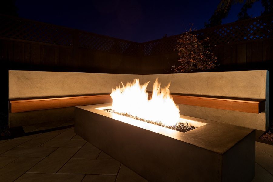 Close view of tall flames in a linear concrete fire table in front of a lit concrete bench at night