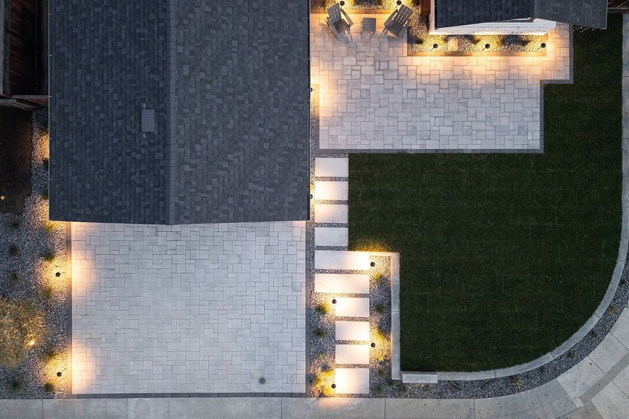 Top-down twilight view of lit stepping slabs, a paver driveway and a curved lawn edge with warm path lights