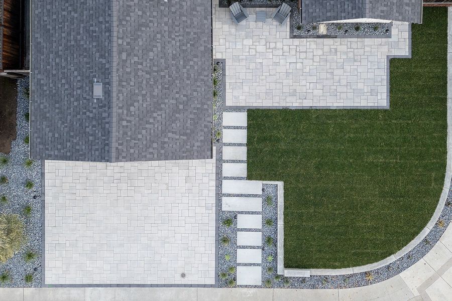 Top-down daytime view of the paver driveway, stepping-slab path, patio and curved curb around the lawn