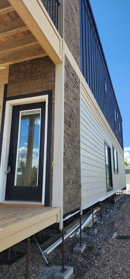 Modular home with stone wainscot, dark siding and a covered porch