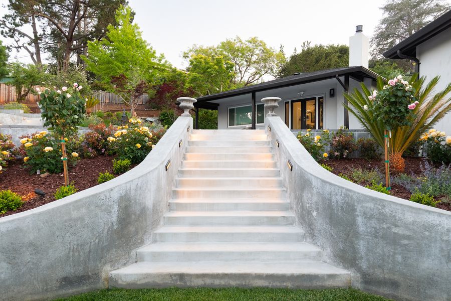 Wide concrete staircase between curved planters, risers lit, climbing to the house