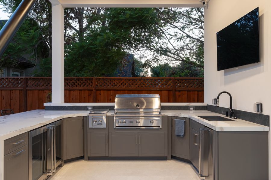 Outdoor kitchen in the cabana — grill, sink, cabinetry and a wall-mounted screen under a timber ceiling