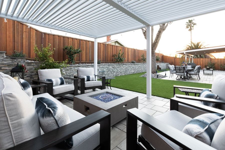 Looking out from under the pergola past a fire table and sofas over a turf lawn to a second covered patio